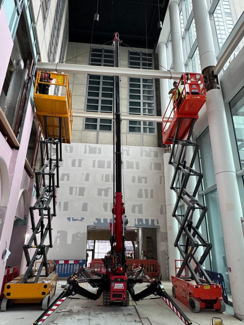 Fully electric spider crane lifting a steel beam indoors, London