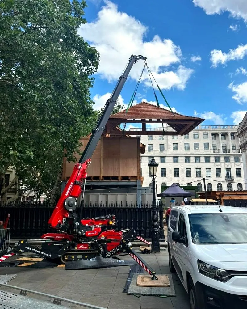 Red spider crane lifting a timber gazebo roof into place in central London